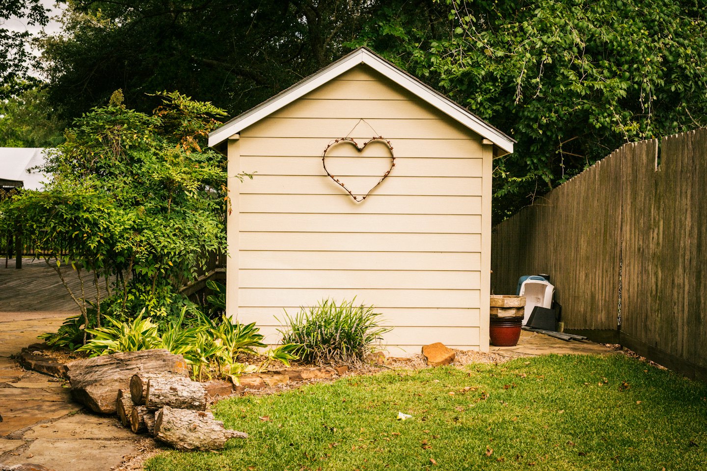 A backyard shed with a heart decoration stands in a garden.
