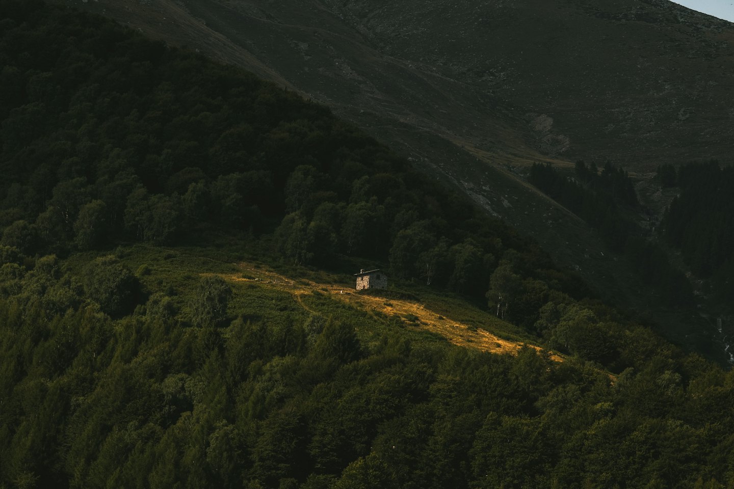 A small stone cabin sits on a grassy mountain hillside.