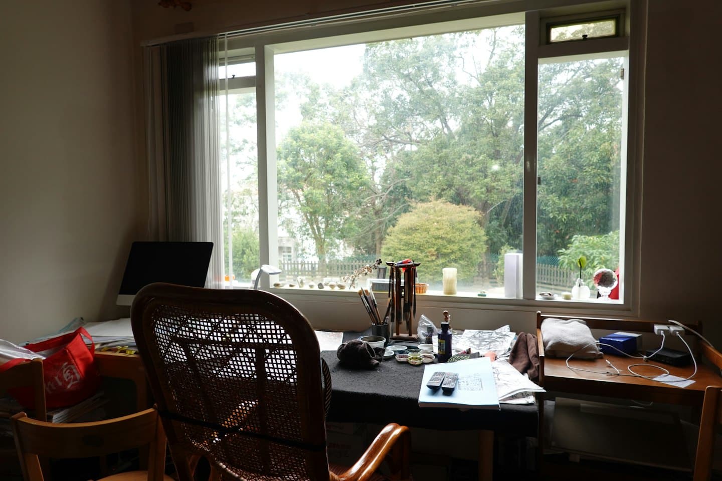 A cluttered desk with art supplies facing a garden window.